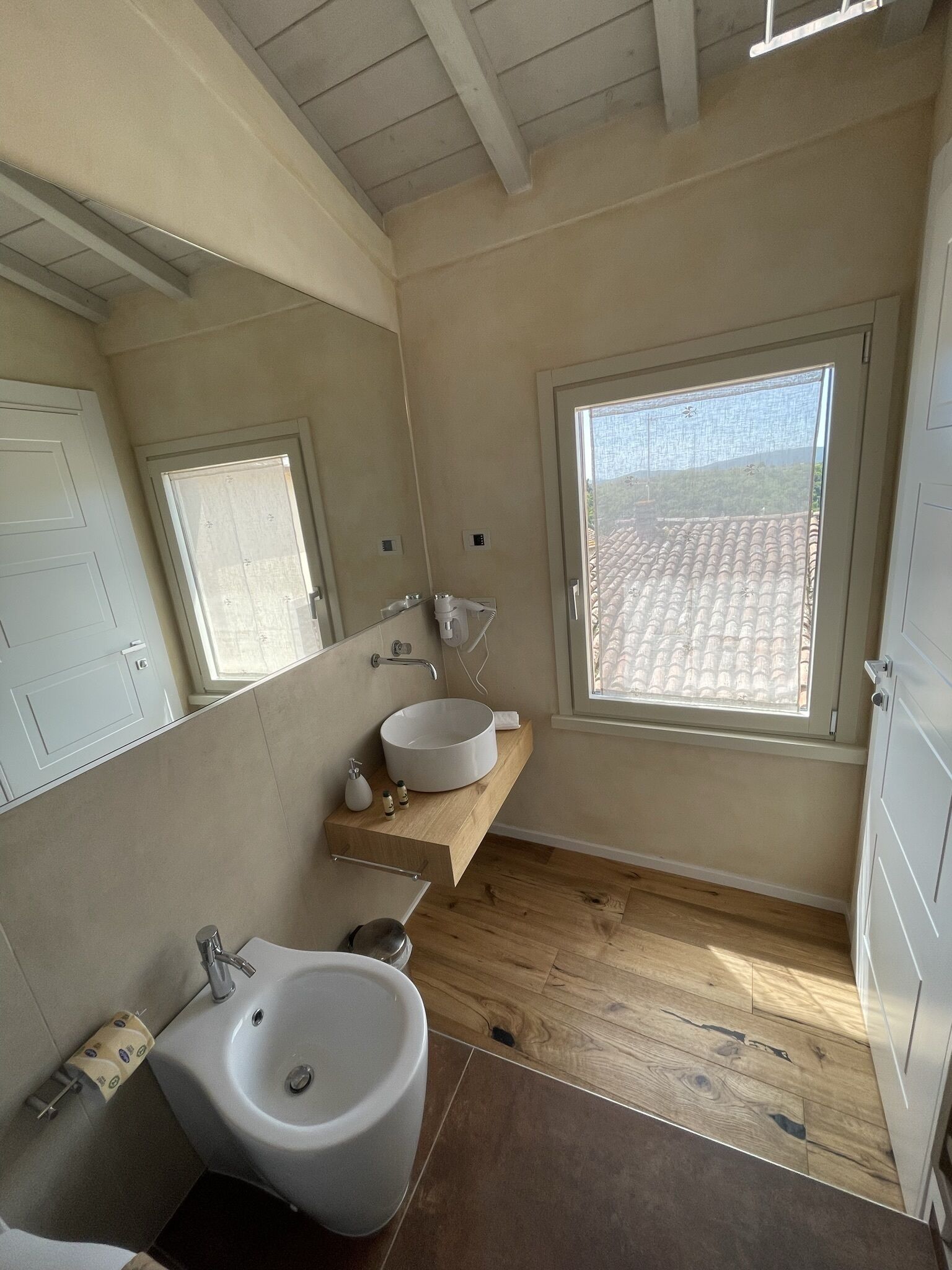 Un baño moderno con un espejo grande, un lavabo redondo y una ventana con vistas al tejado.