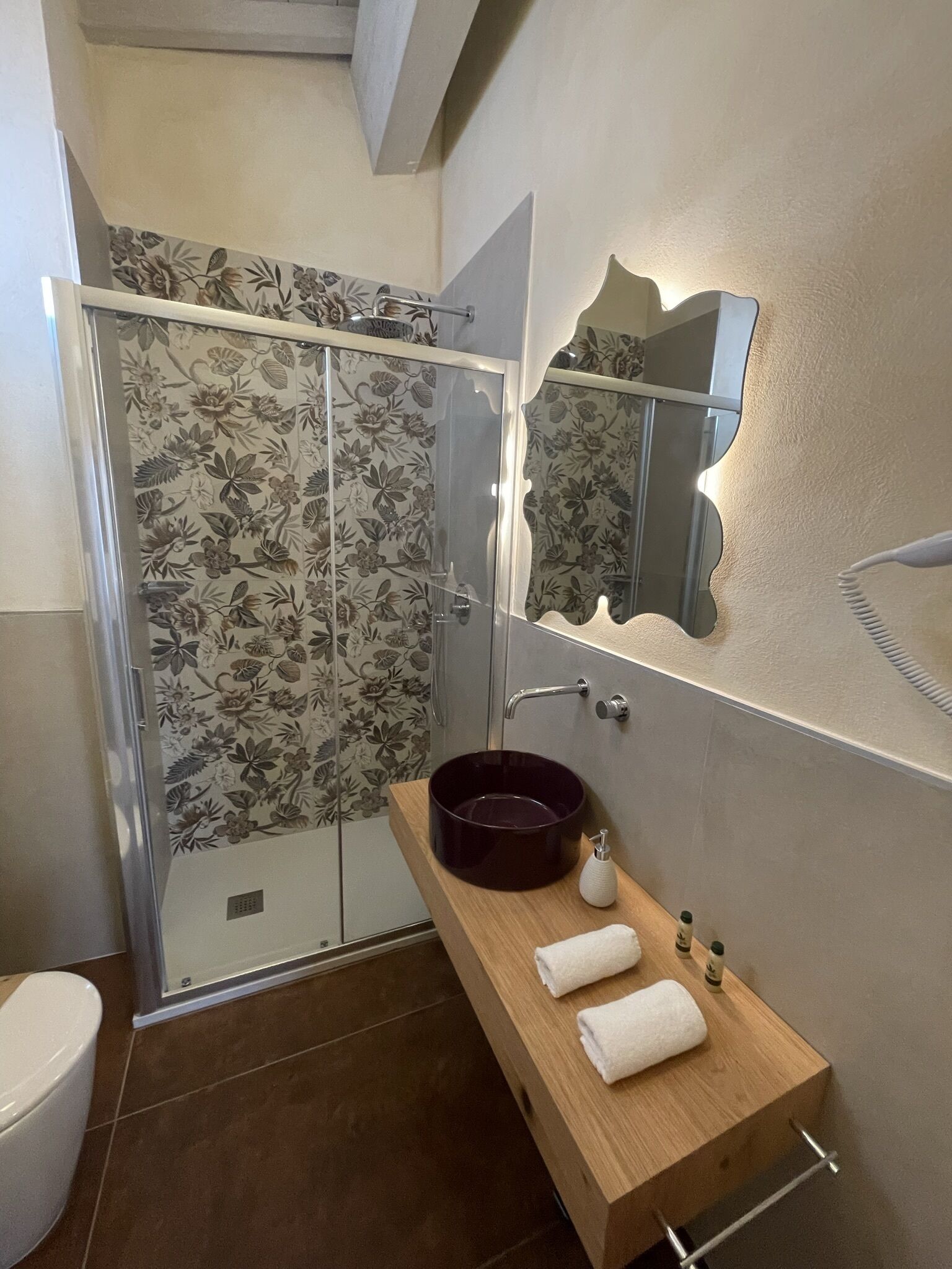 Une salle de bain avec une douche, un meuble-lavabo en bois avec un vasque de couleur foncée, un miroir et un porte-serviettes.