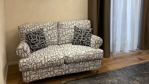 Una sala de estar con un sofá estampado, un tapete oscuro y un ventanal con cortinas.
