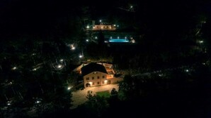 A large, two-story building with a swimming pool, surrounded by trees and illuminated by night lights. - Dream House (Arezzo)