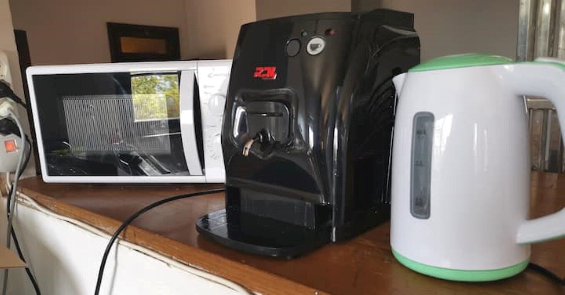A coffee maker, a mug, and a microwave on a wooden countertop.