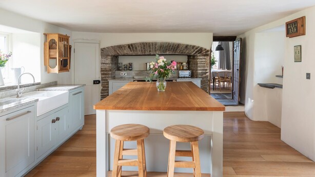 Una cocina amplia con una isla central, taburetes de madera, un arco de piedra y vistas al comedor.