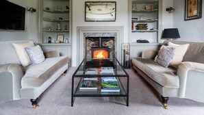 Sala de estar con dos sofás, una mesa de centro de vidrio con libros, una chimenea y estantes con objetos decorativos.