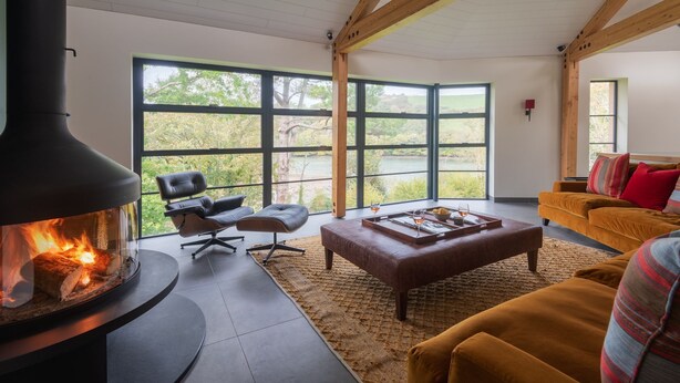 Un salon moderne doté d’une grande cheminée, de sièges confortables et de larges fenêtres offrant une vue sur l’extérieur.