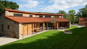 Une maison moderne avec une façade en pierre, de grandes fenêtres et un patio couvert aménagé avec du mobilier d’extérieur.