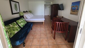 Quarto compacto com cama, escrivaninha e cadeira. Há uma televisão fixada na parede e um quadro pendurado acima da escrivaninha.
