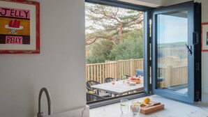 A kitchen with a large window, a sink, and a table with a tray of fruit and glasses. - Murrawingi -  a beautiful modern coastal home (Salcombe)