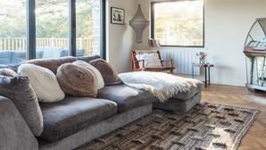 A cozy living room with a grey sofa, a patterned rug, and a view of the outdoors through large windows. - Murrawingi -  a beautiful modern coastal home (Salcombe)