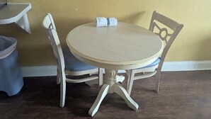 Una mesa redonda con mantel blanco, dos sillas blancas y una toalla blanca doblada sobre la mesa.