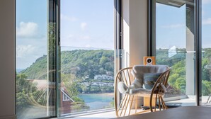 Ein Zimmer mit einem großen Fenster, das Blick auf einen Hügel und einen Strand bietet. Ein bequemer Holzstuhl steht in der Nähe des Fensters.