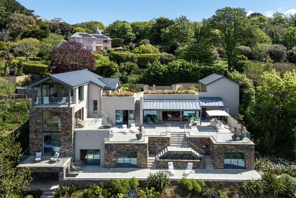 Ein modernes Haus mit Wintergarten, einer Stein-Fassade und einer Dachterrasse mit Gartenmöbeln.