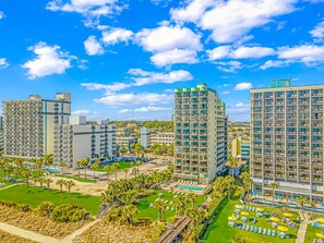 A high-rise hotel with multiple balconies, a pool area, and a well-maintained lawn.