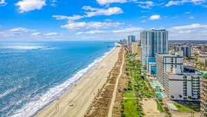 Un paysage urbain côtier avec une plage, des immeubles de grande hauteur et un ciel dégagé.