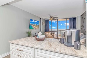 A modern kitchen with a marble countertop, a coffee maker, and a view of the ocean.