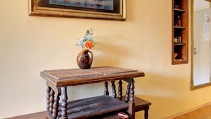 Une pièce comprenant une table en bois, une chaise, un petit meuble, un tableau encadré accroché au mur et un vase avec des fleurs.