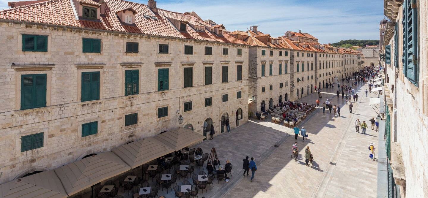 A courtyard with stone buildings, green shutters, and outdoor seating.