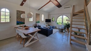A spacious living area with a dining table, sofa, and a wooden staircase. - Luxe Appartement met 2 Slaapkamers, Groot Terras Direct aan Zwembad La Mourre 16 (Le Plan-de-la-Tour)