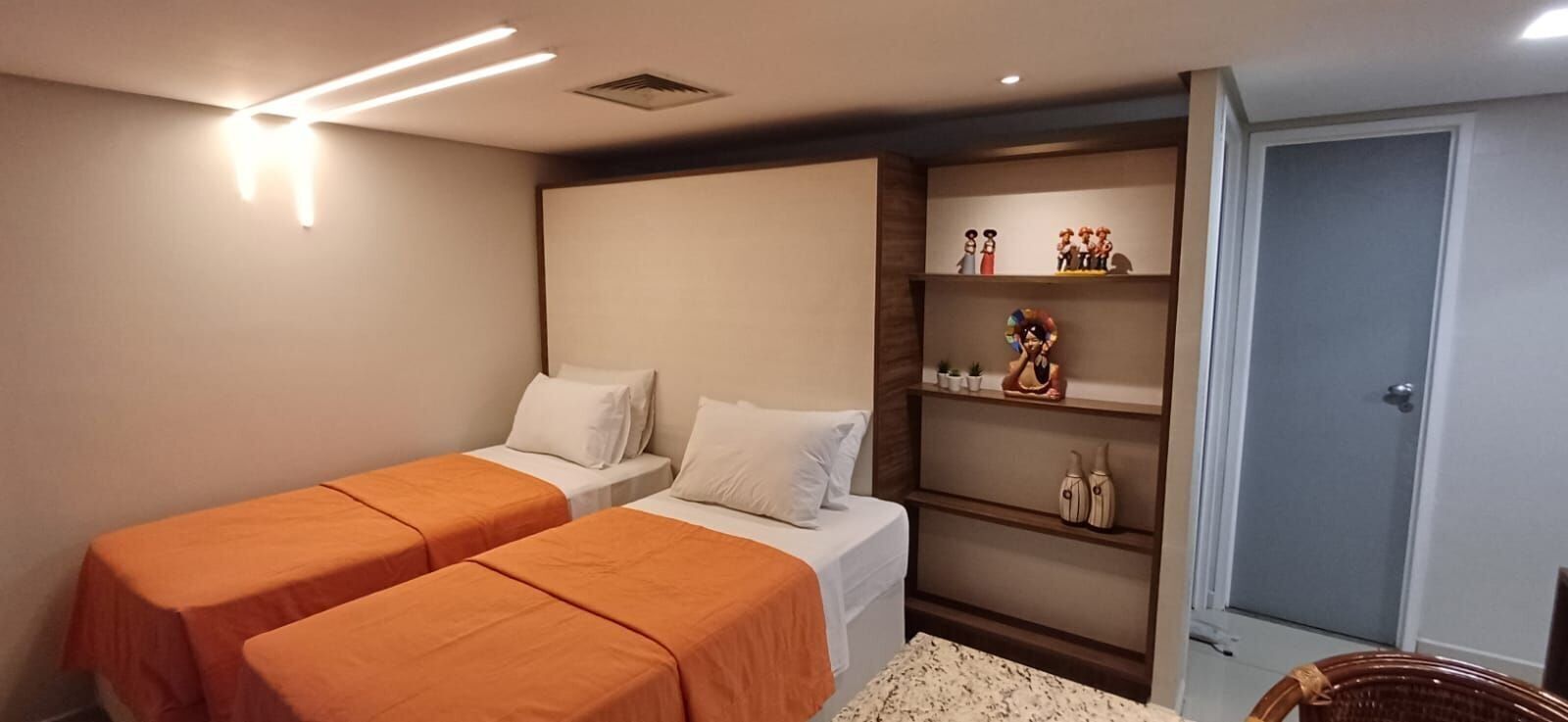 A room with two beds, a shelf with decorative items, and a door.