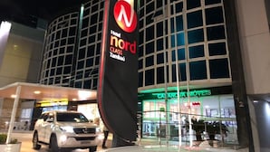 A hotel entrance with a prominent sign for 'Nord Class Tambatu,' a glass storefront with 'CASA MÓVETS' signage, and a white vehicle parked in front. - Imperial Suítes (João Pessoa)