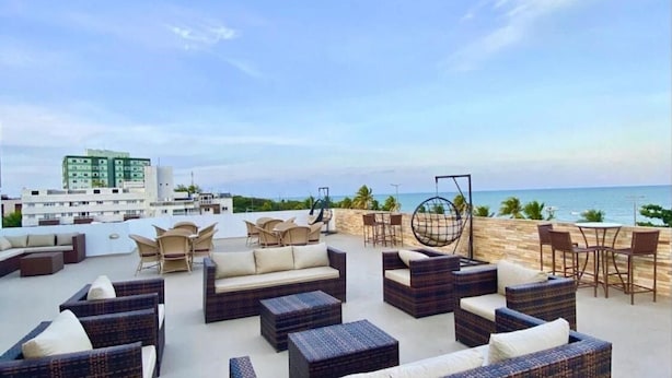 A rooftop terrace with outdoor seating, a swing chair, and a view of the ocean. - Imperial Suítes (João Pessoa)