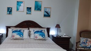 A bedroom with a wooden headboard, two nightstands, a bed with a patterned bedspread, and four framed marine life pictures on the wall.