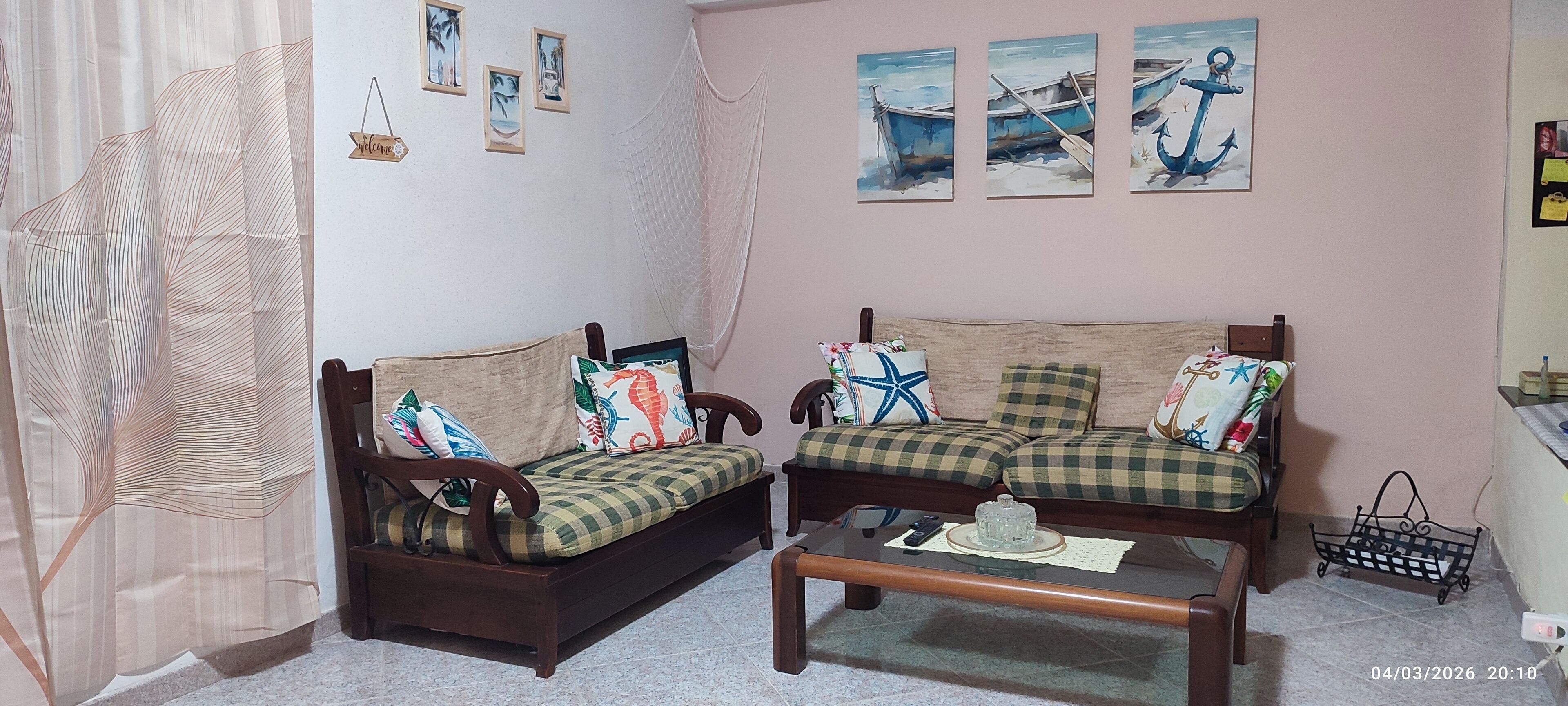 A cozy living room with two wooden sofas, a coffee table, and nautical-themed wall art.