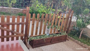 A wooden gate with a chain lock, a gravel pathway, and a wooden planter box with green plants.