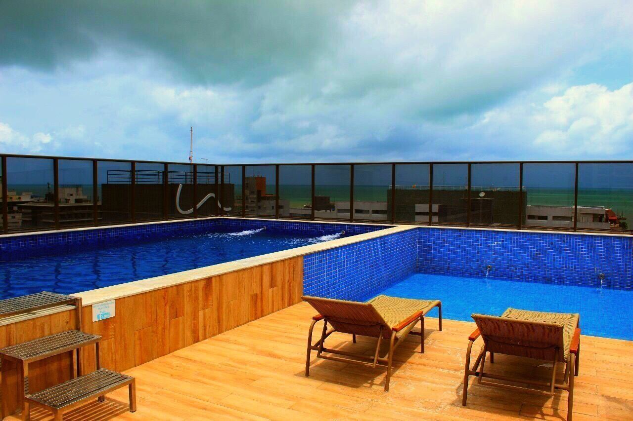 Une piscine sur le toit offrant une vue sur l’océan, une terrasse en bois et des chaises longues.