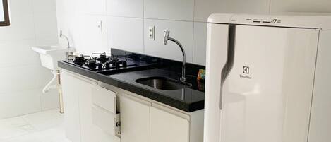 Una cucina moderna con mobili bianchi, un piano di lavoro nero, un lavello in acciaio inossidabile e un frigorifero bianco.