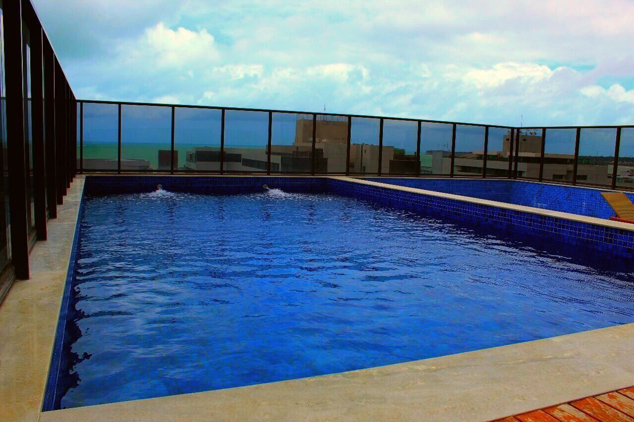 A rooftop infinity pool with a clear view of the ocean and buildings in the background.
