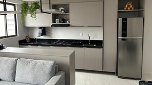 A modern kitchen with a central island, built-in appliances, and a minimalist design. - Compact Flat Tambau (João Pessoa)