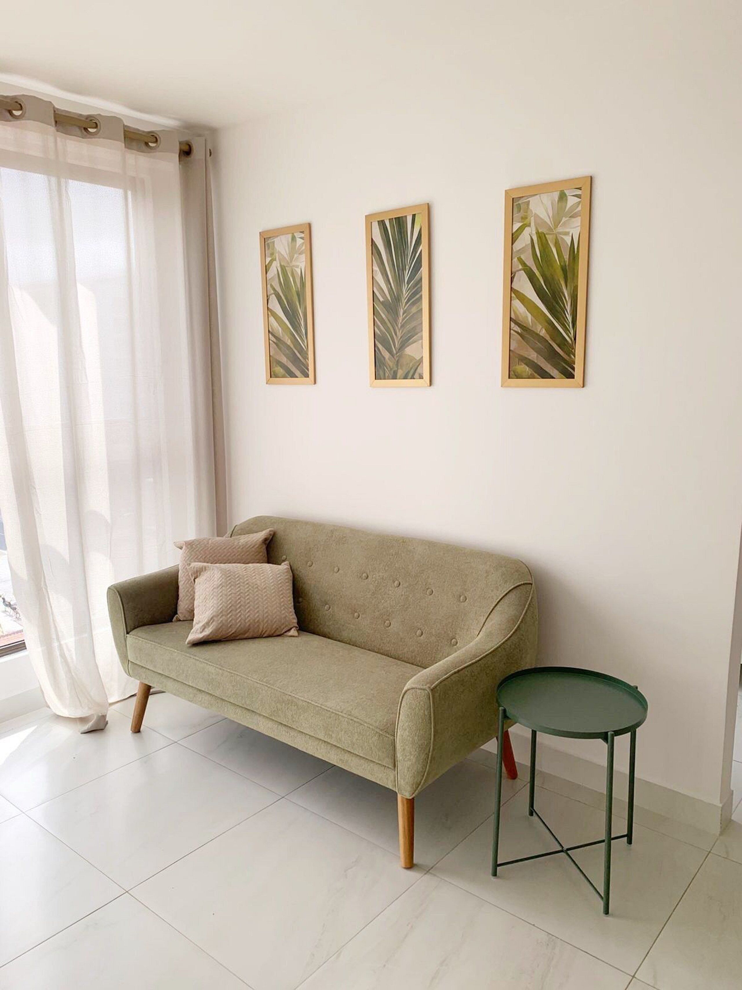A living room with a beige sofa, a small green table, and three framed botanical prints on the wall.