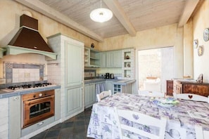 Een keuken met een gasfornuis, oven en lichtblauwe kastjes. Er staat een eettafel met een bloemistisch tafelkleed.