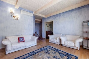 Een woonkamer met twee witte banken, een vloerkleed met blauw patroon en een houten plafond.