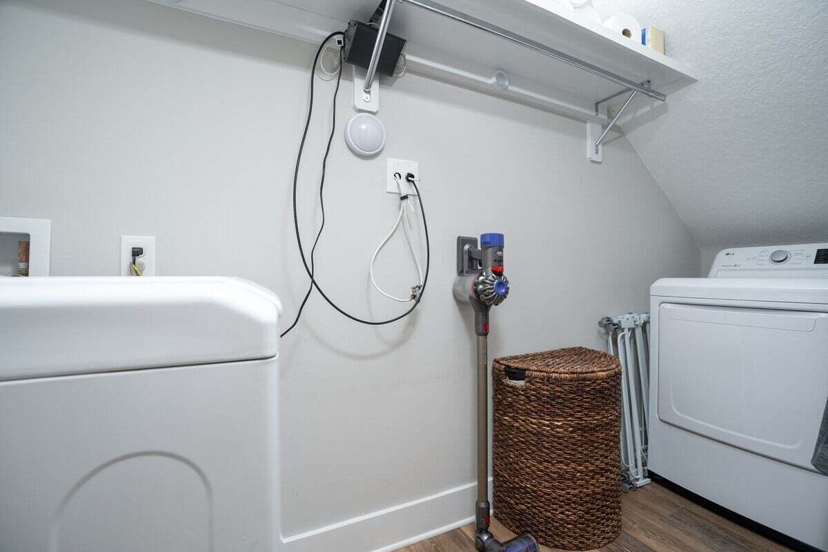 Une buanderie équipée d’un lave-linge, d’un sèche-linge et d’un enrouleur de tuyau avec un panier.