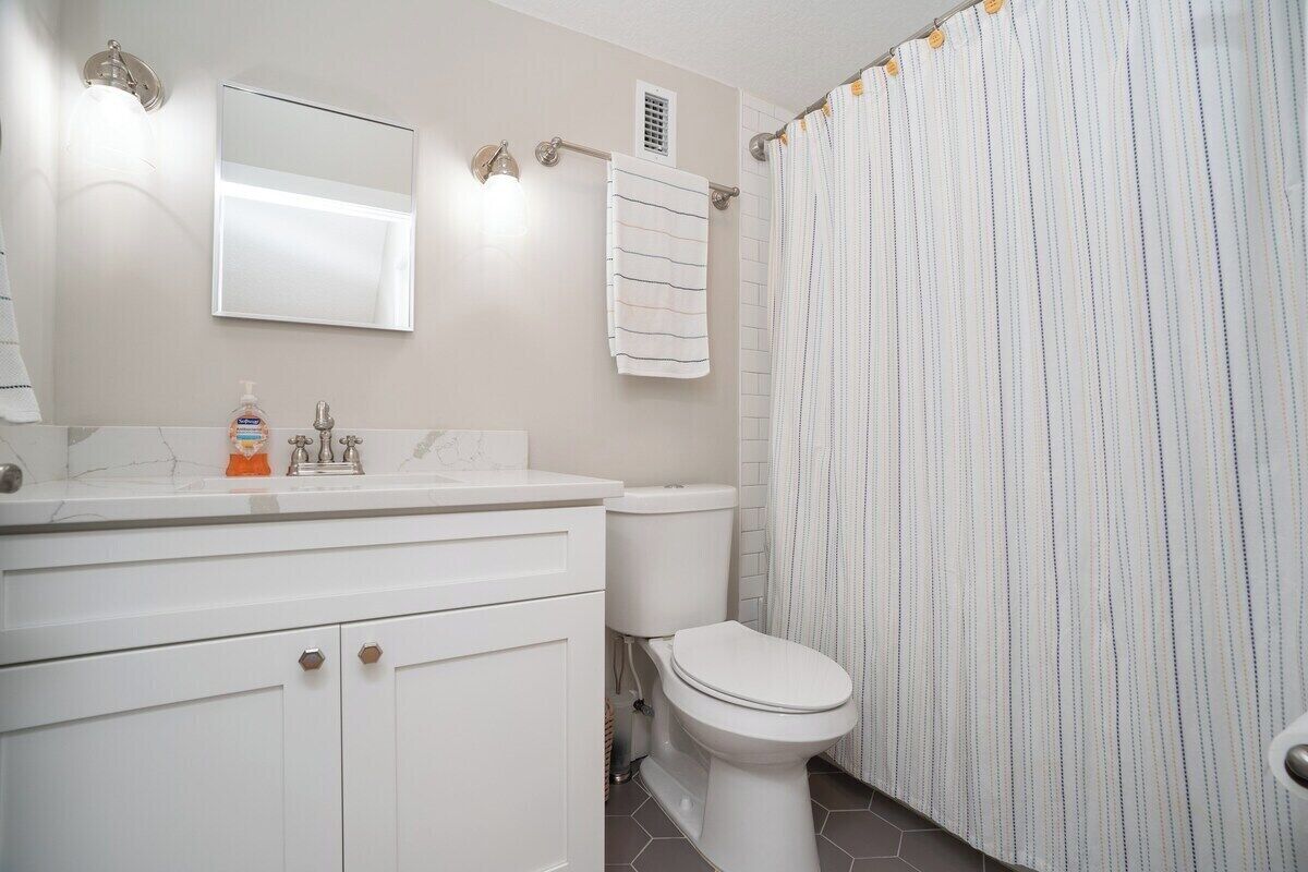 Une salle de bain avec un meuble-lavabo blanc, des toilettes, un miroir et un rideau de douche à rayures.