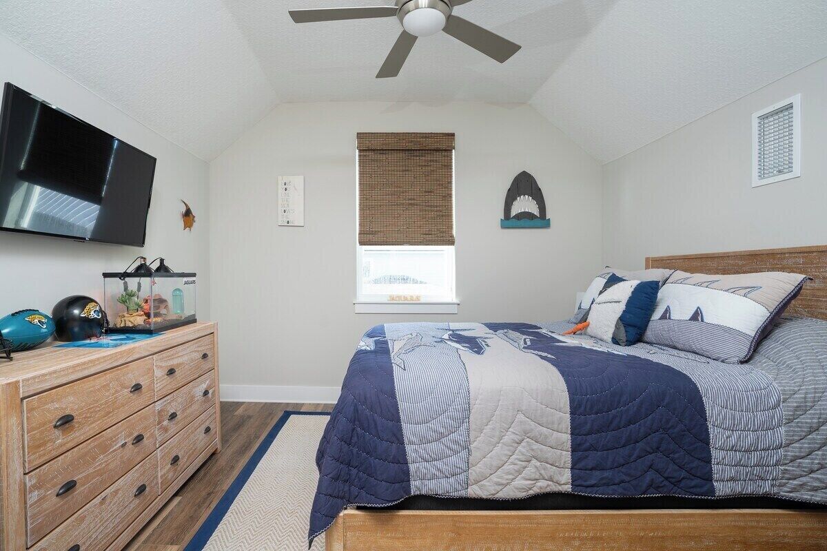 Een slaapkamer met een bed, een houten dressoir, een televisie en een plafondventilator.