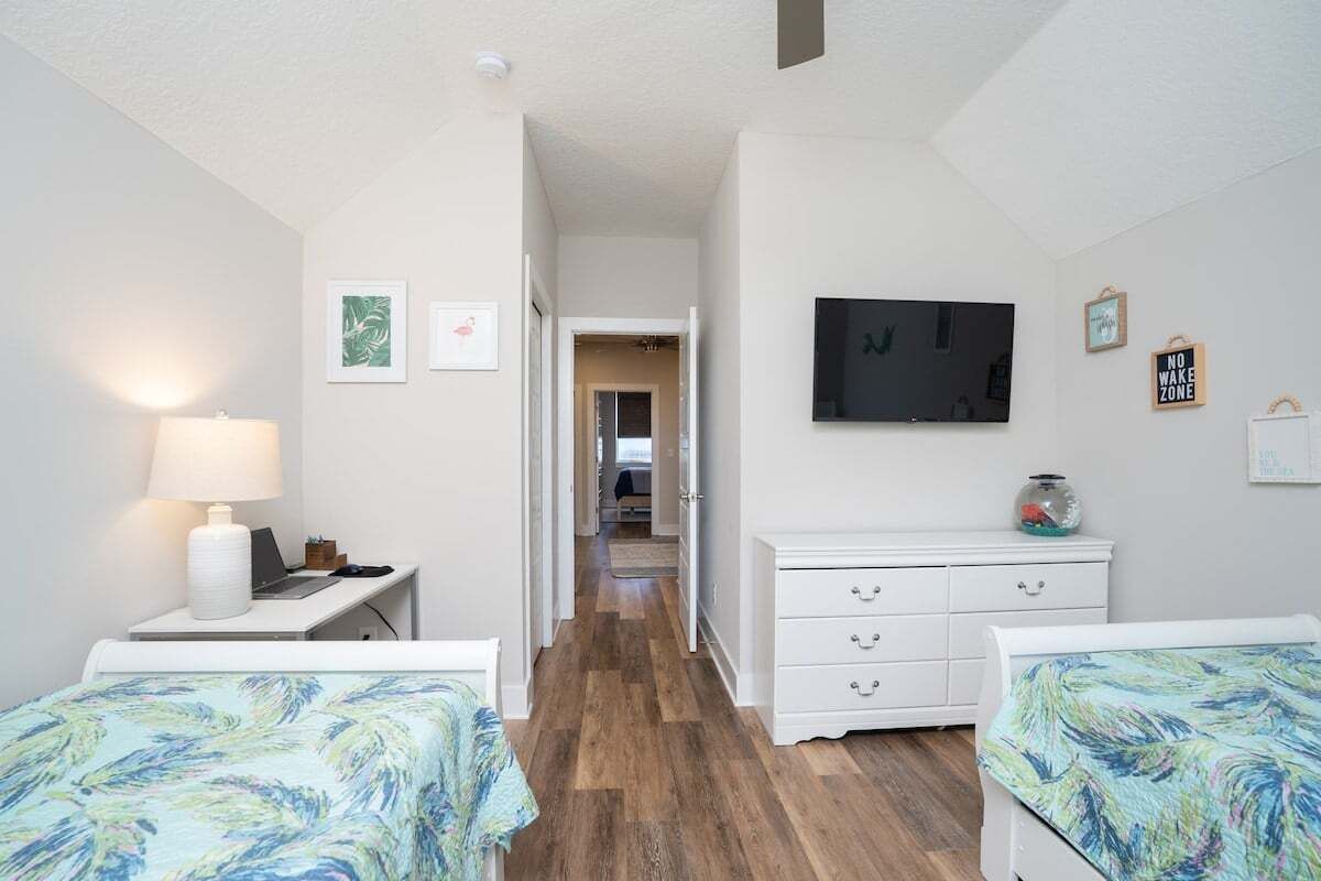 A bedroom with two beds, a desk with a lamp, a TV, and a dresser.