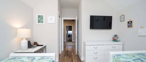 A bedroom with two beds, a desk with a lamp, a TV, and a dresser.