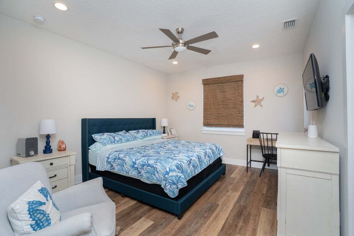 A bedroom with a bed, a desk, a chair, a ceiling fan, and a TV.