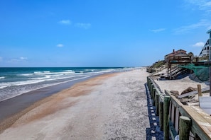 A beach with a wooden walkway leading to a building with a balcony overlooking the ocean. - Coastal Sol|Heated Pool|6-min to BCH|Golf Cart (Vilano Beach)