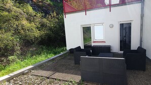 An outdoor seating area with wicker furniture, a white building with two doors, and a red safety railing. - Ferienwohnung Zentrale Lage (Idar-Oberstein)