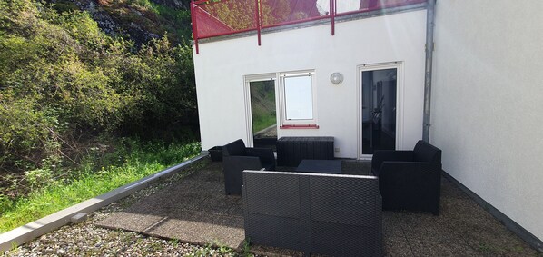 An outdoor seating area with wicker furniture, a white building with two doors, and a red safety railing.