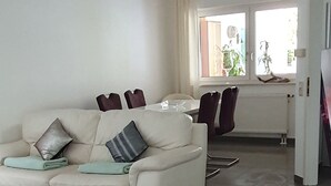 A modern living room with a white sofa, a dark rug, and a view of the outdoors through a window. - Ferienwohnung Zentrale Lage (Idar-Oberstein)