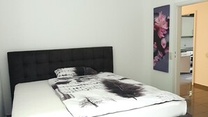 A bedroom with a bed, a headboard, a wall with a floral painting, and a door leading to another room. - Ferienwohnung Zentrale Lage (Idar-Oberstein)