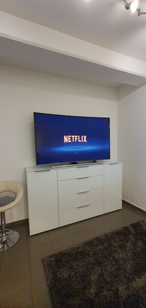 A modern living room with a flat-screen TV mounted on a white cabinet, a small round table, and a dark area rug.