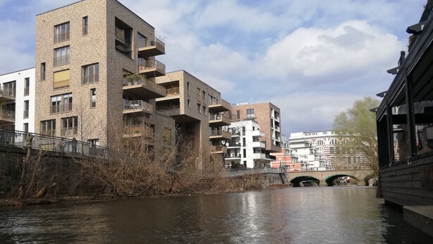 Un bâtiment situé au bord de la rivière, doté de nombreux balcons, avec un pont en arrière-plan.