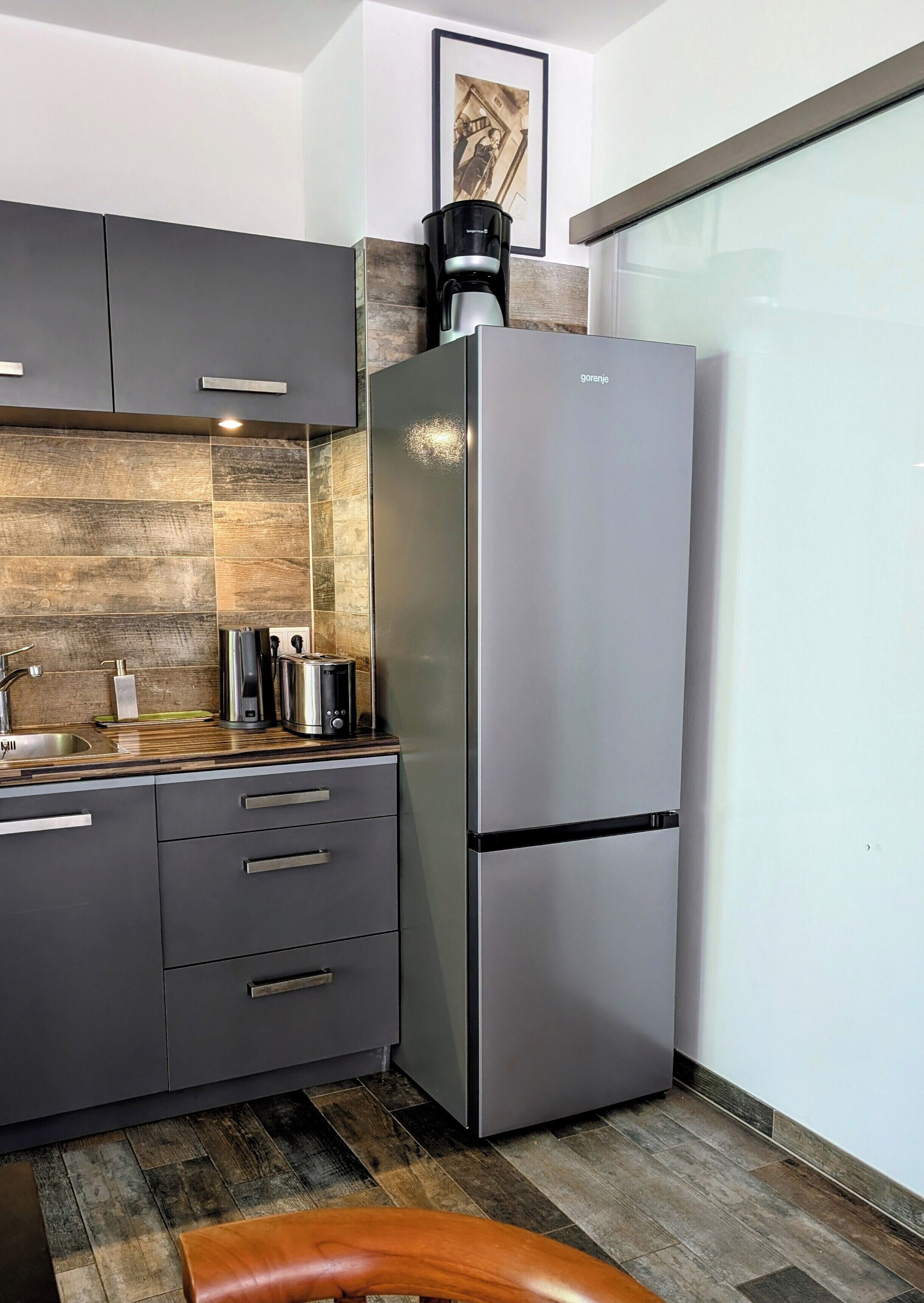 A modern kitchen with a stainless steel refrigerator, wooden countertop, and grey cabinets.