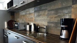 Une cuisine moderne dotée d’un plan de travail foncé, d’appareils électroménagers en acier inoxydable et d’un pare-feu en bois.