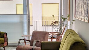 Un salon moderne avec un canapé vert, une table basse en bois et un fauteuil rose. On aperçoit une plante en pot sur une table en bois, ainsi qu’un tableau accroché au mur.